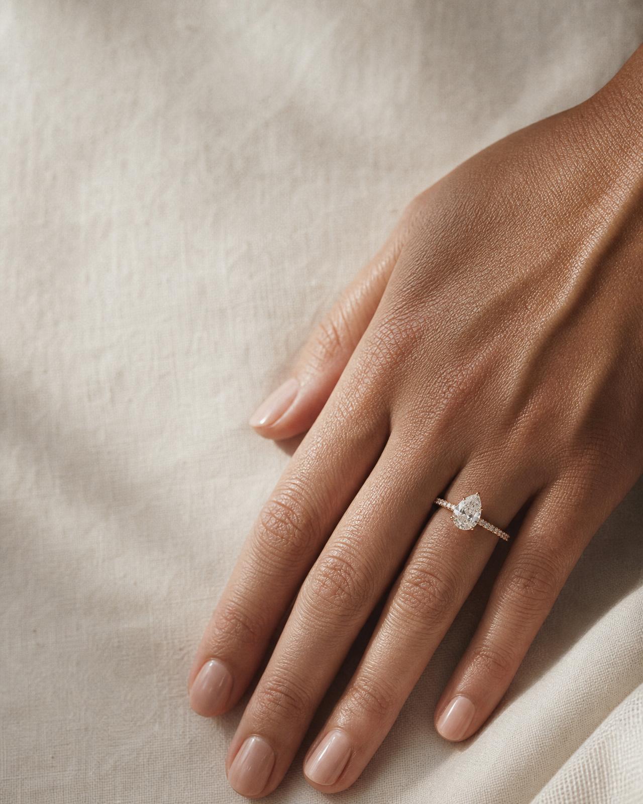 Close-up of a woman's hand wearing a pear-cut halo diamond engagement ring, size 6½