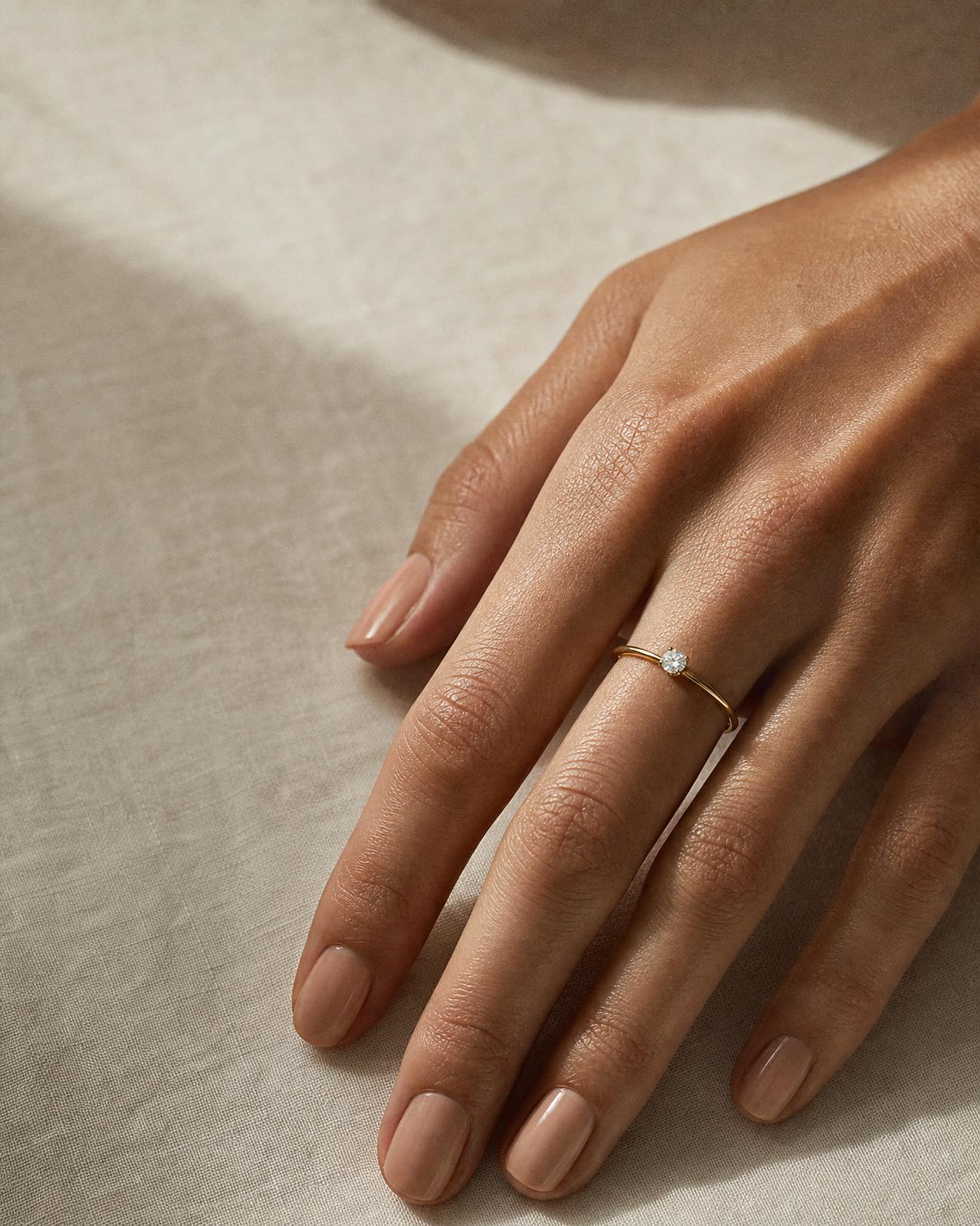 Close-up of a woman's hand wearing a round solitaire diamond engagement ring on the ring finger, size 6½